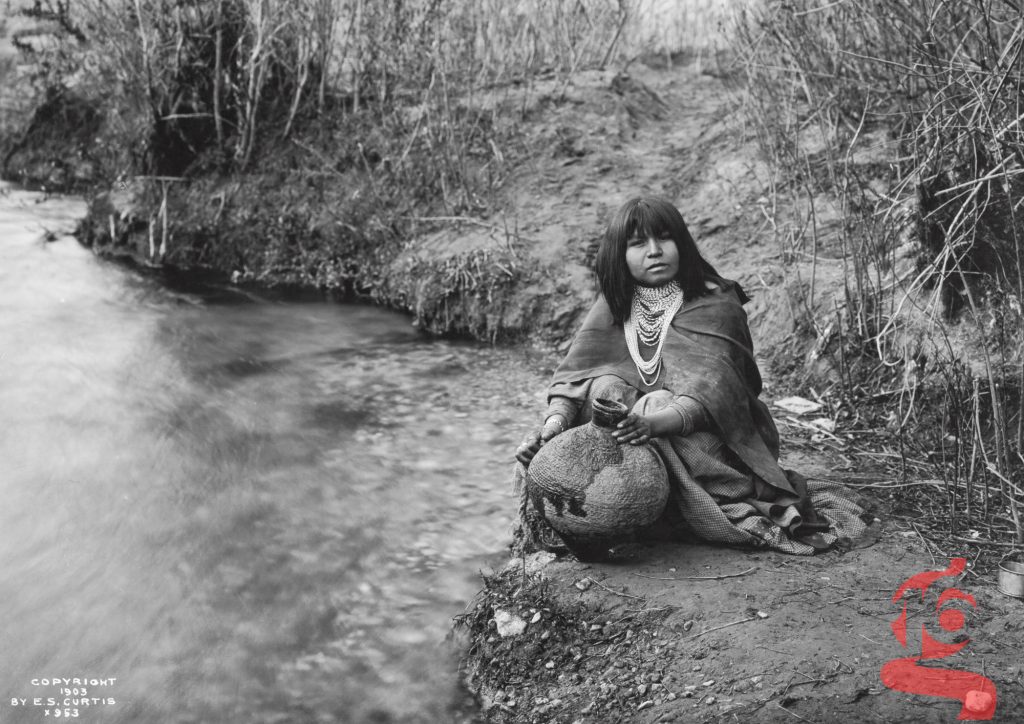 Femme acoma assise près d’un cours d’eau avec une jarre, photographiée par Edward S. Curtis en 1903.