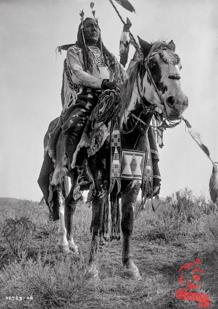 Bird On the Ground, homme Apsáalooke à cheval richement paré, photographié par Edward S. Curtis en 1908.