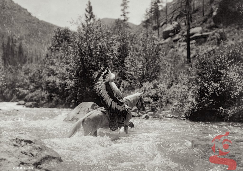 Bullchief, homme Crow à cheval portant une coiffe de plumes et traversant une rivière, photographié par Edward S. Curtis vers 1905