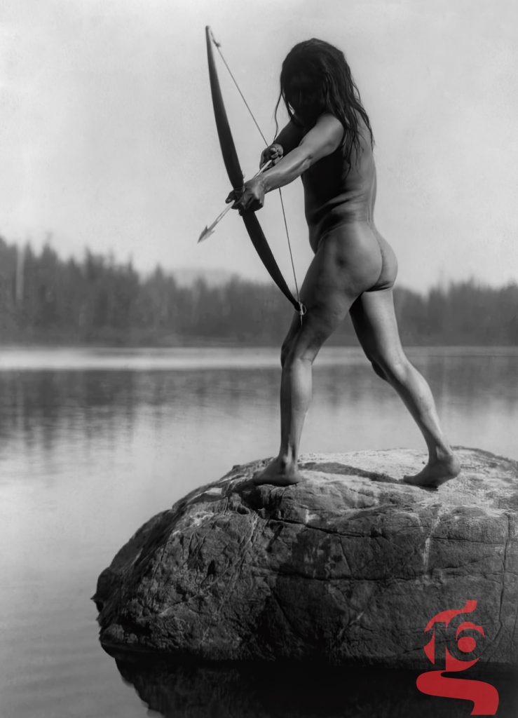 Archer Nuu-chah-nulth tendant son arc sur un rocher au bord d’un lac, photographié par Edward S. Curtis en 1915.