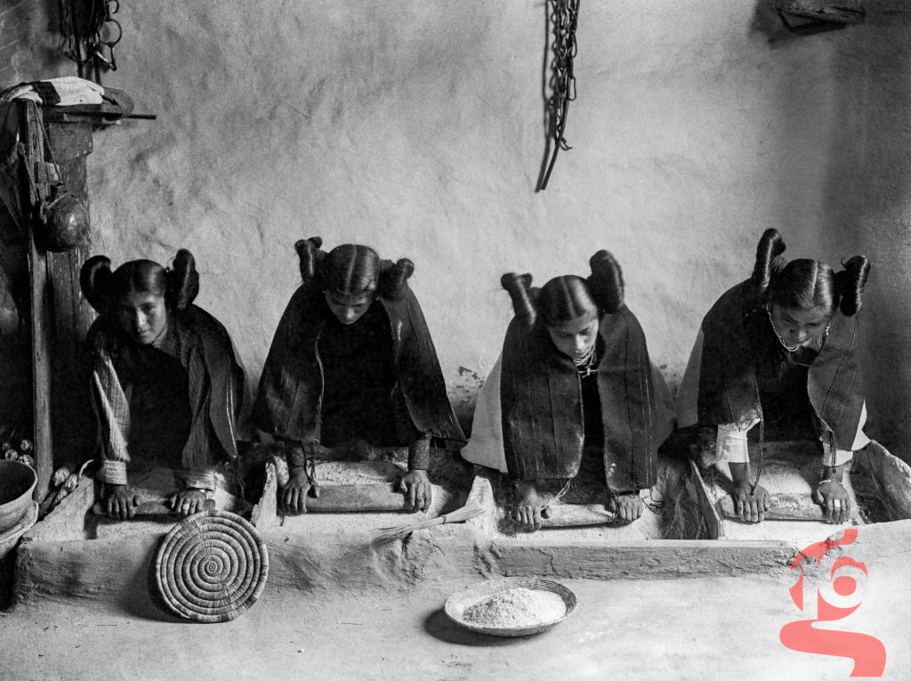 Quatre jeunes femmes hopies broyant le maïs dans une auge, photographiées par Edward S. Curtis en 1906.
