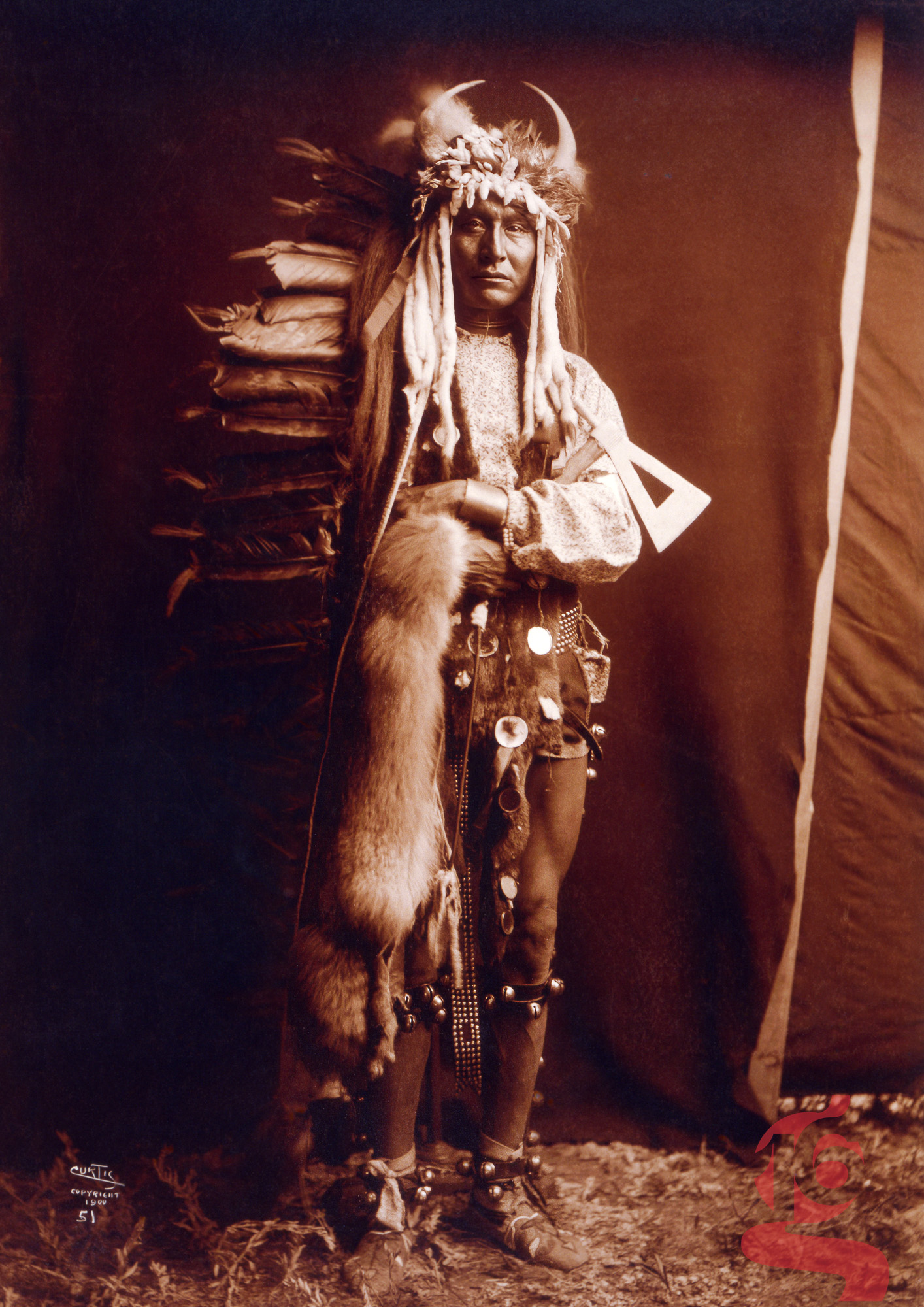 Portrait en pied d’Iron Breast, homme Piegan en tenue cérémonielle ornée de plumes, fourrure et cornes, photographié par Edward S. Curtis en 1900.