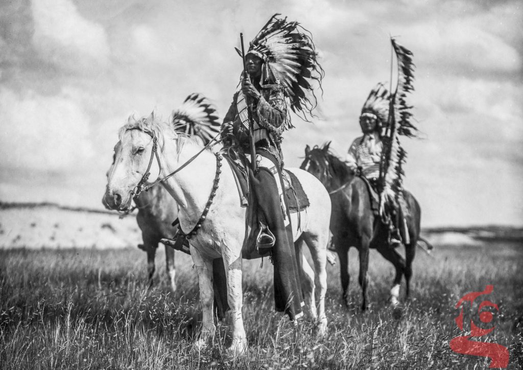 Trois chefs piegan portant des coiffes de plumes et montés à cheval dans la prairie, photographie d’Edward S. Curtis de 1900.